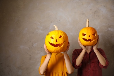 Photo of Women with pumpkin heads against beige background, space for text. Jack lantern - traditional Halloween decor