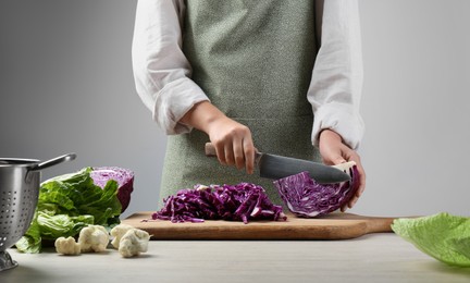 Photo of Woman cutting fresh radicchio cabbage on board at wooden table, closeup