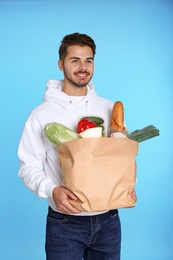 Young man holding paper bag with products on color background. Food delivery service