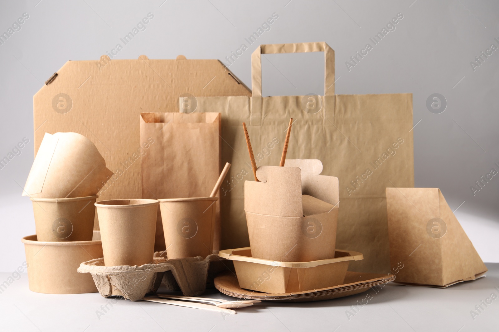 Photo of Eco friendly food packaging. Paper containers, tableware and bag on light background