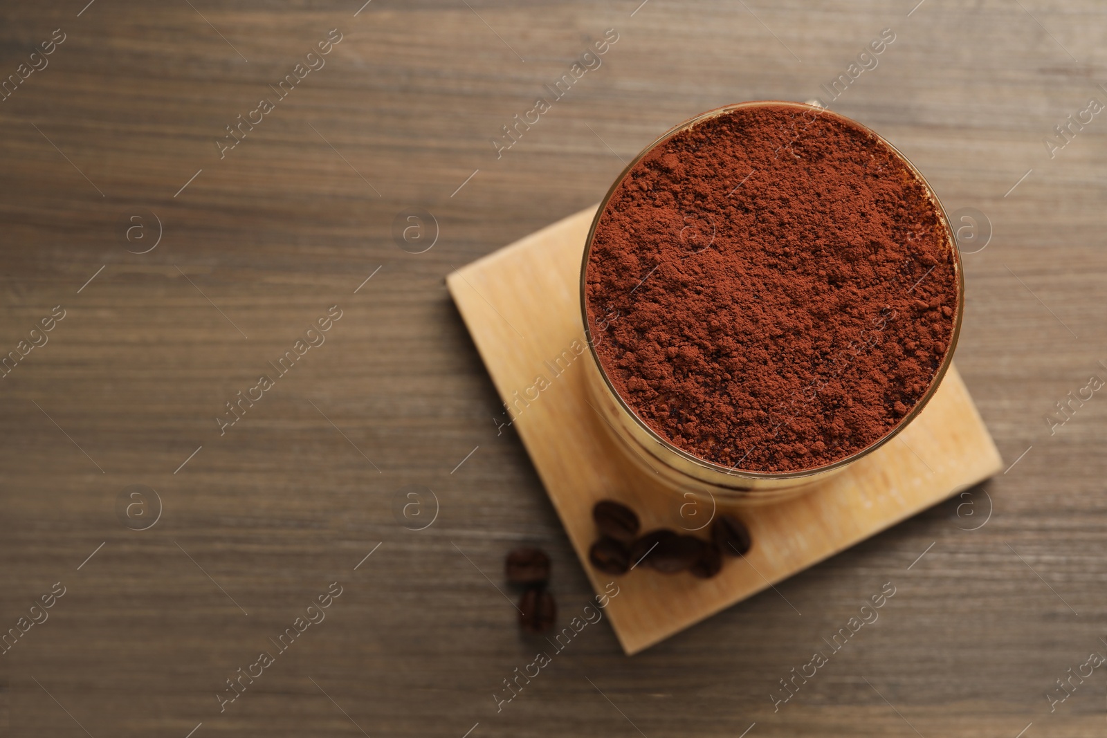 Photo of Delicious tiramisu in glass and coffee beans on wooden table, top view. Space for text