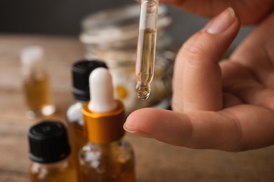 Woman applying essential oil on finger over table, closeup. Space for text