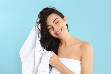 Photo of Young woman drying hair with towel on light blue background