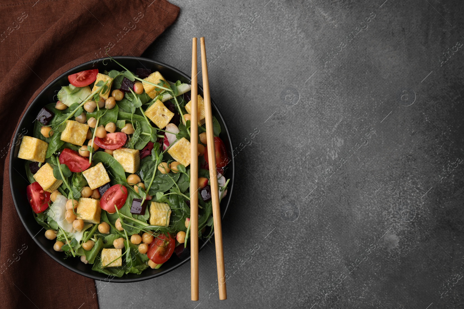 Photo of Bowl of tasty salad with tofu, chickpeas and vegetables on brown textured table, top view. Space for text