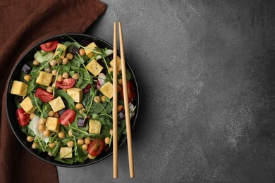 Bowl of tasty salad with tofu, chickpeas and vegetables on brown textured table, top view. Space for text