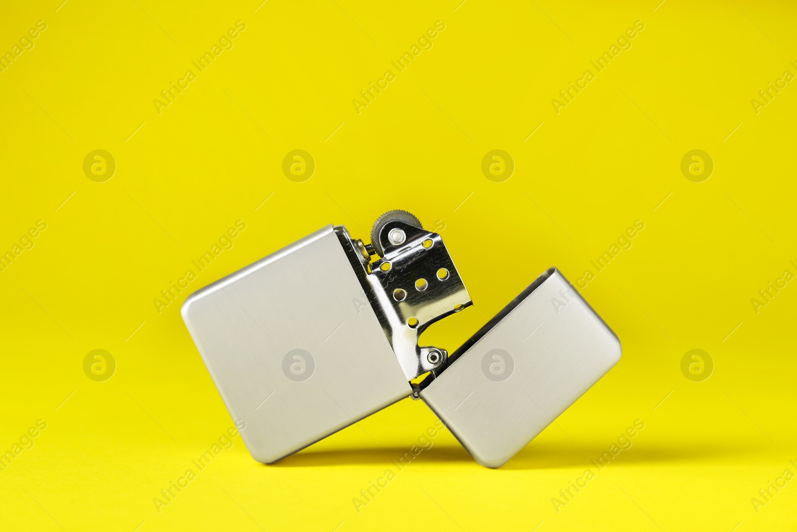 Photo of Gray metallic cigarette lighter on yellow background, closeup