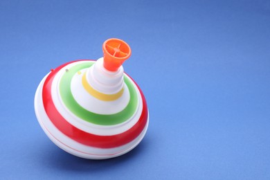 Photo of One bright spinning top on blue background, closeup with space for text. Toy whirligig
