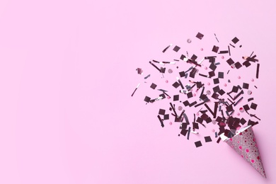 Photo of Shiny silver confetti bursting out of party cracker on pink background, top view. Space for text