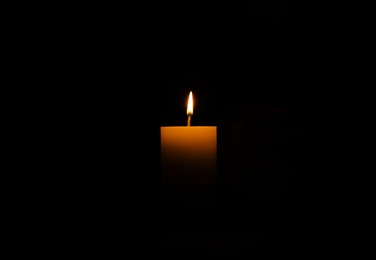 One burning wax candle on black background