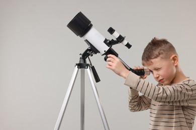 Photo of Little boy looking at stars through telescope on light grey background, space for text