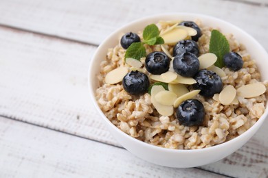 Photo of Tasty oatmeal with blueberries, mint and almond petals in bowl on wooden table, closeup. Space for text