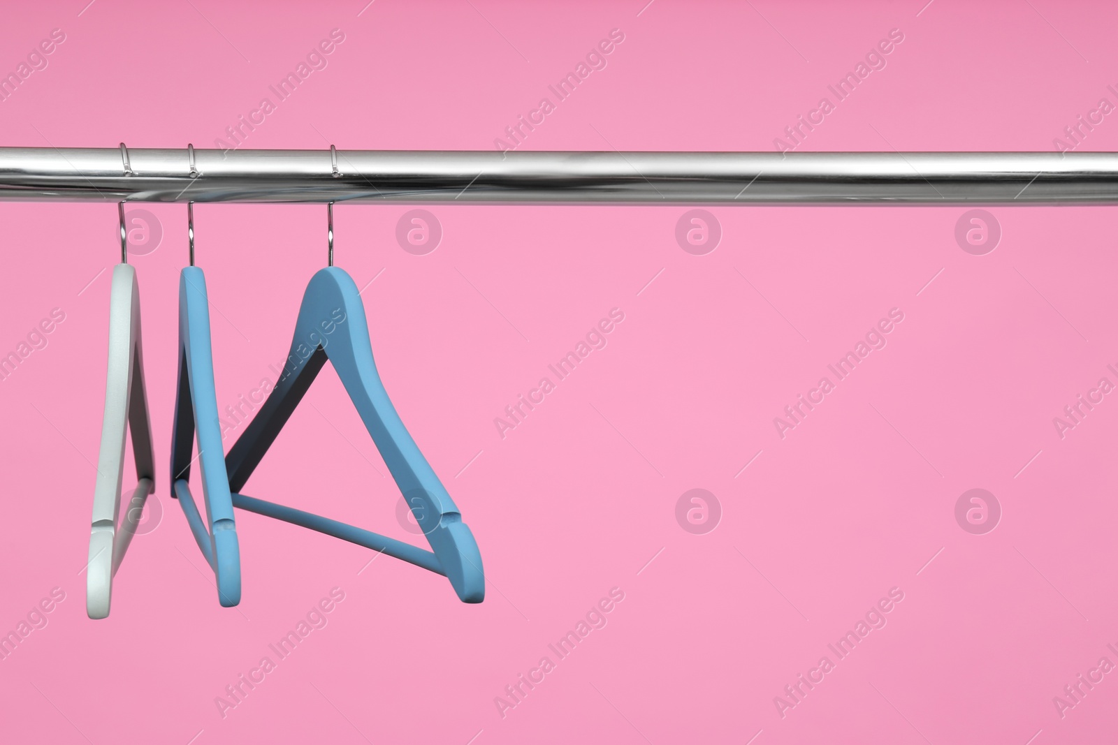 Photo of Empty clothes hangers on metal rail against color background. Space for text