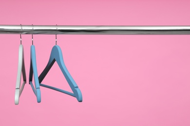 Photo of Empty clothes hangers on metal rail against color background. Space for text