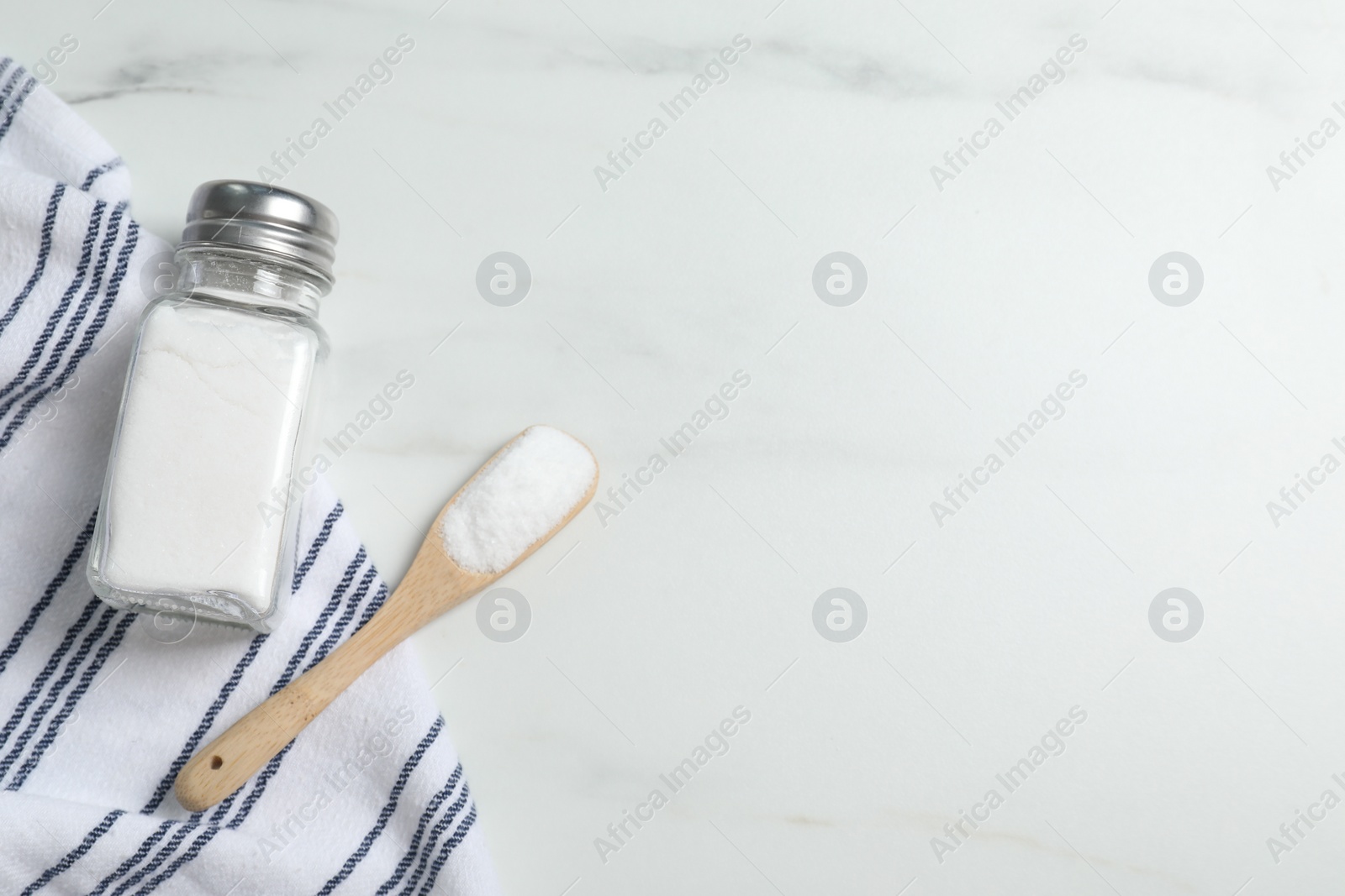 Photo of Shaker with salt on white marble table, flat lay. Space for text