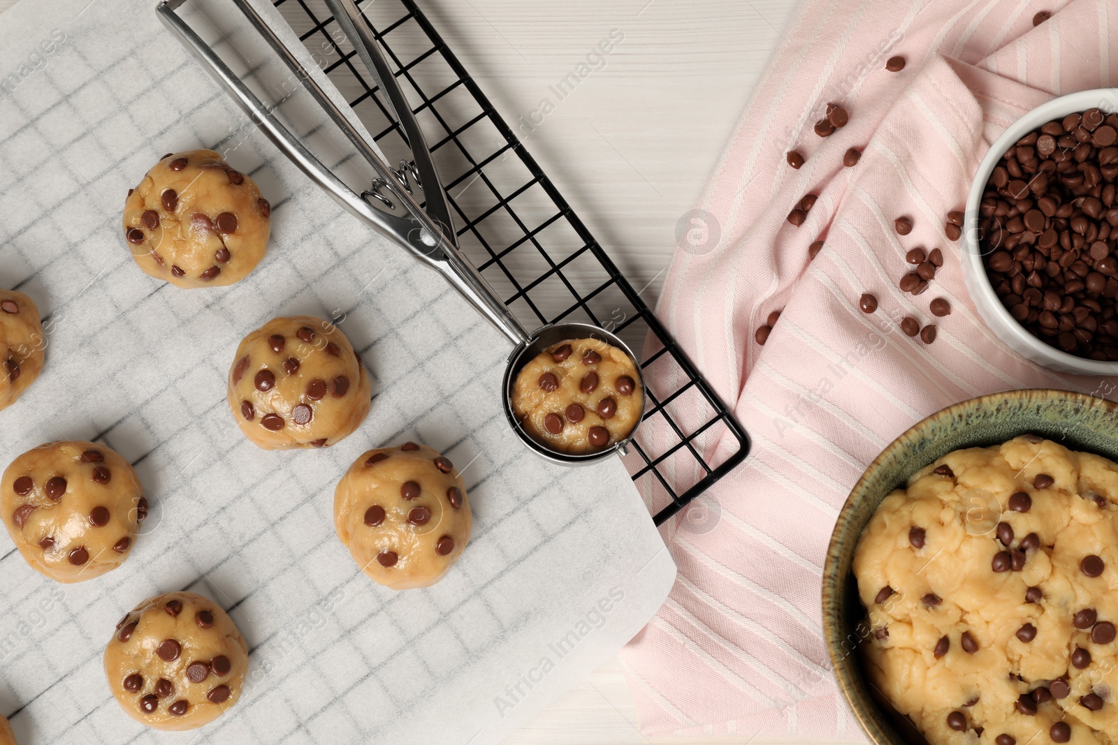 Photo of Bowl with dough and uncooked chocolate chip cookies on white wooden table, flat lay