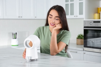 Woman enjoying air flow from portable fan in kitchen. Summer heat