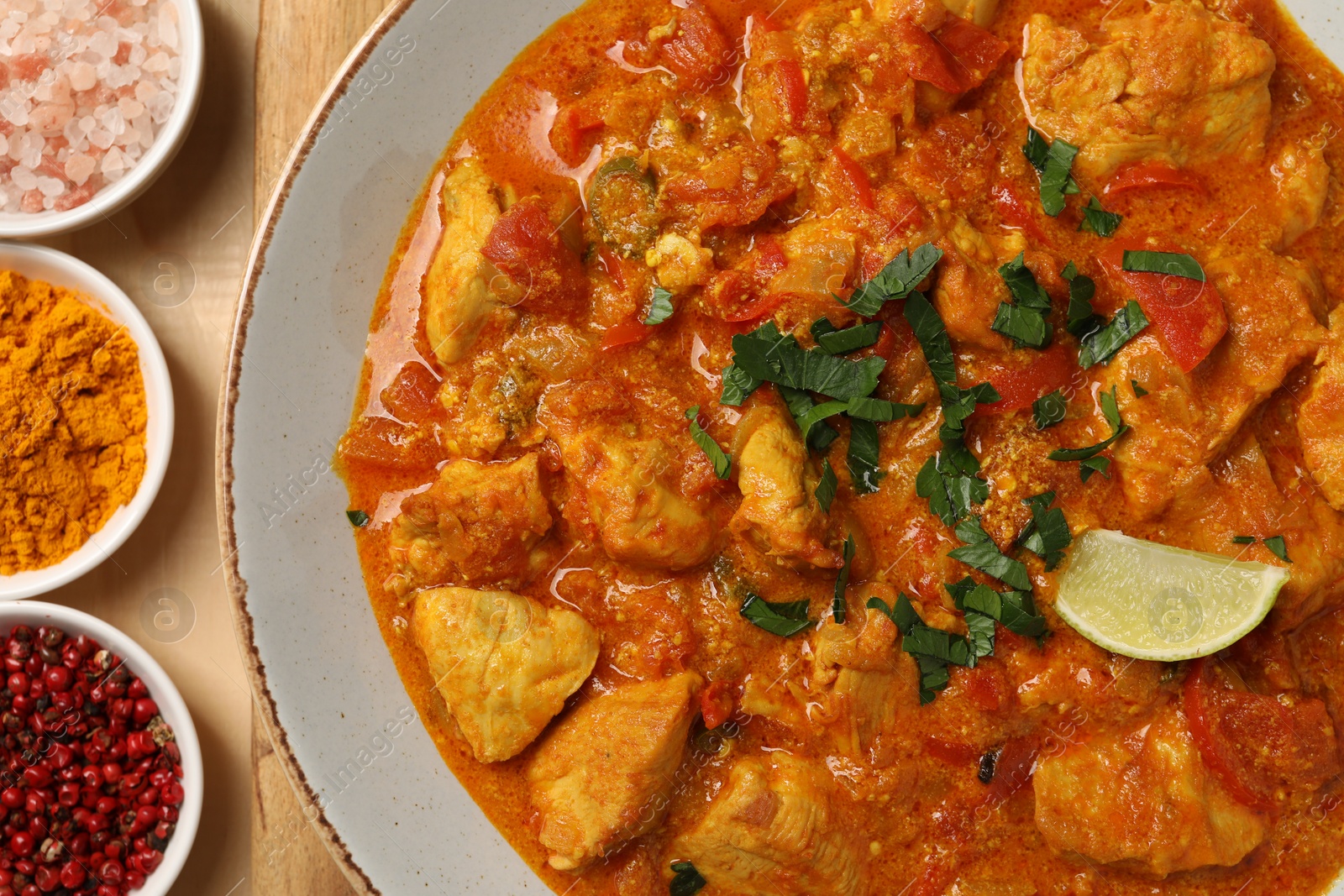 Photo of Delicious chicken curry and spices on wooden table, flat lay