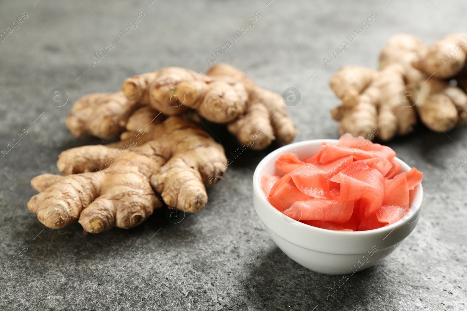 Photo of Spicy pickled ginger and root on grey table, closeup