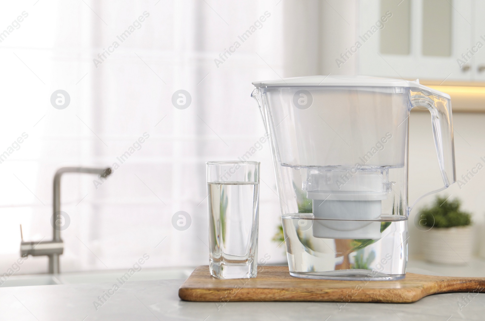 Photo of Water filter jug and glass on light table in kitchen. Space for text