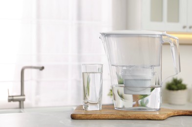 Photo of Water filter jug and glass on light table in kitchen. Space for text