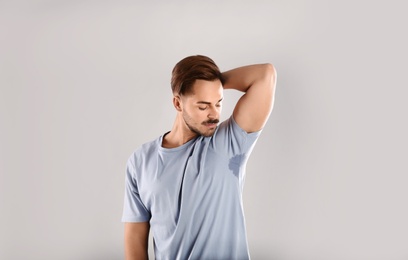 Photo of Sweaty man with stain on t-shirt against gray background. Using deodorant