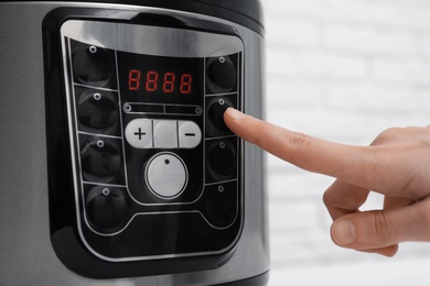Photo of Woman turning on modern electric multi cooker, closeup