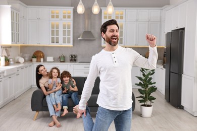 Photo of Happy family having fun at home. Father dancing while his relatives resting on sofa