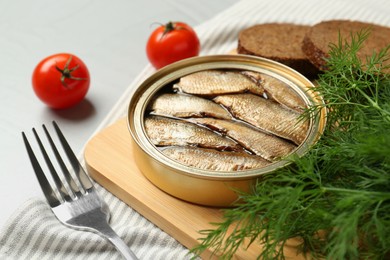 Canned sprats, dill, tomatoes and fork on light table, closeup