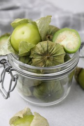 Fresh green tomatillos with husk in glass jar on light table, closeup