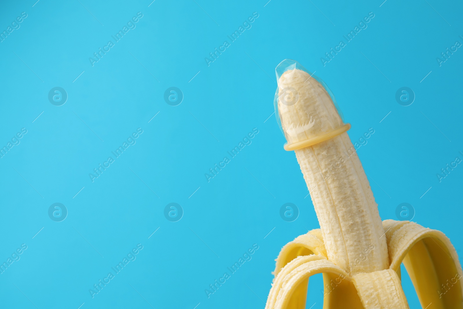 Photo of Banana with condom on light blue background, space for text. Safe sex concept