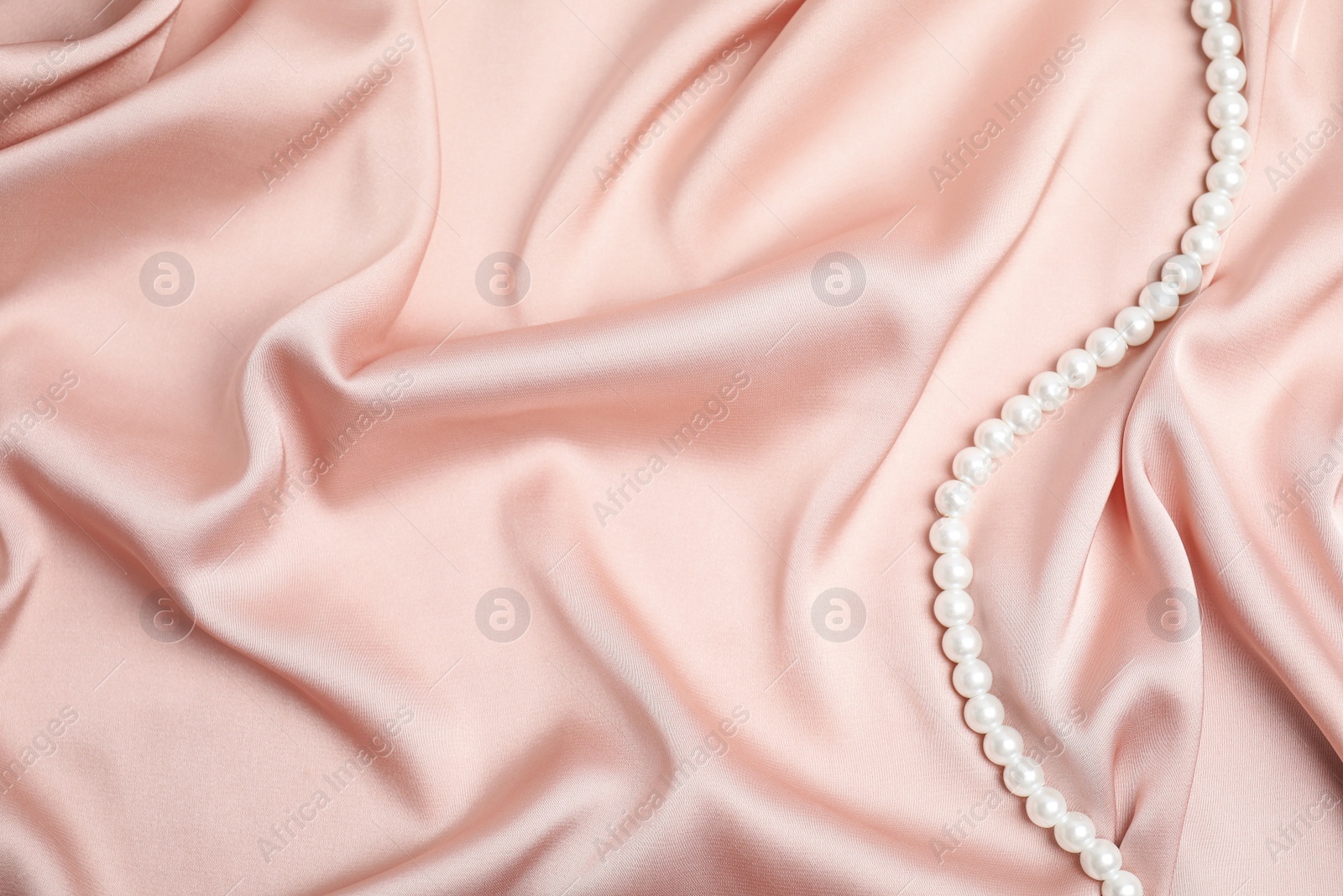 Photo of Beautiful pearls on pink silk, top view. Space for text