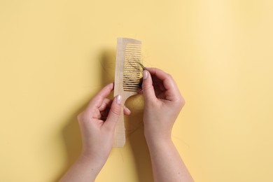 Photo of Woman taking her lost hair from comb on yellow background, top view