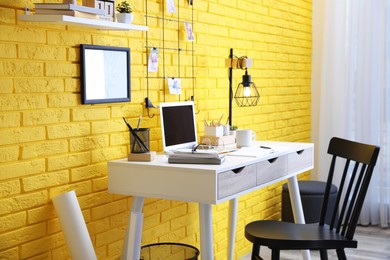 Stylish home office interior with comfortable workplace near yellow brick wall