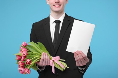 Photo of Man with beautiful bouquet and greeting card on light blue background, closeup