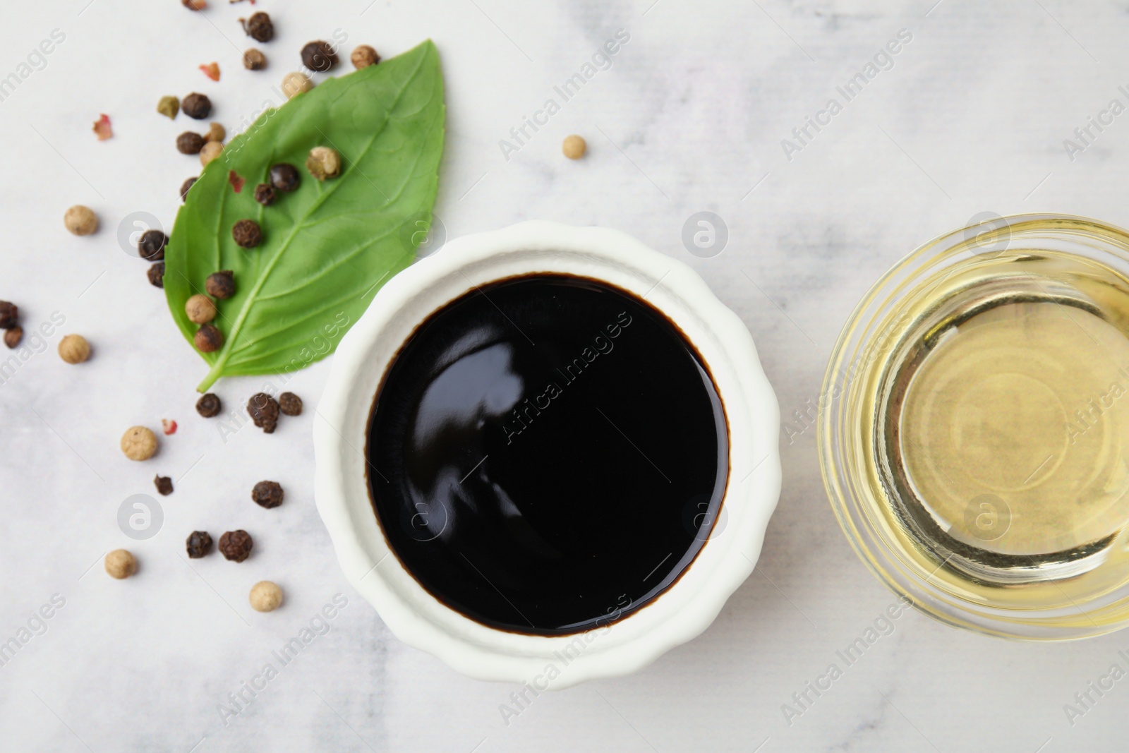 Photo of Bowl with balsamic vinegar and ingredients on white marble table, flat lay