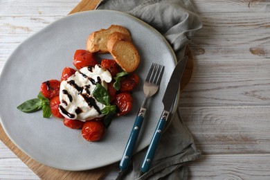 Delicious burrata cheese served with tomatoes, croutons and basil sauce on white wooden table, top view. Space for text