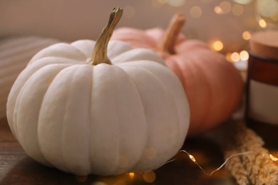 Photo of Two beautiful pumpkins and festive lights indoors, closeup view