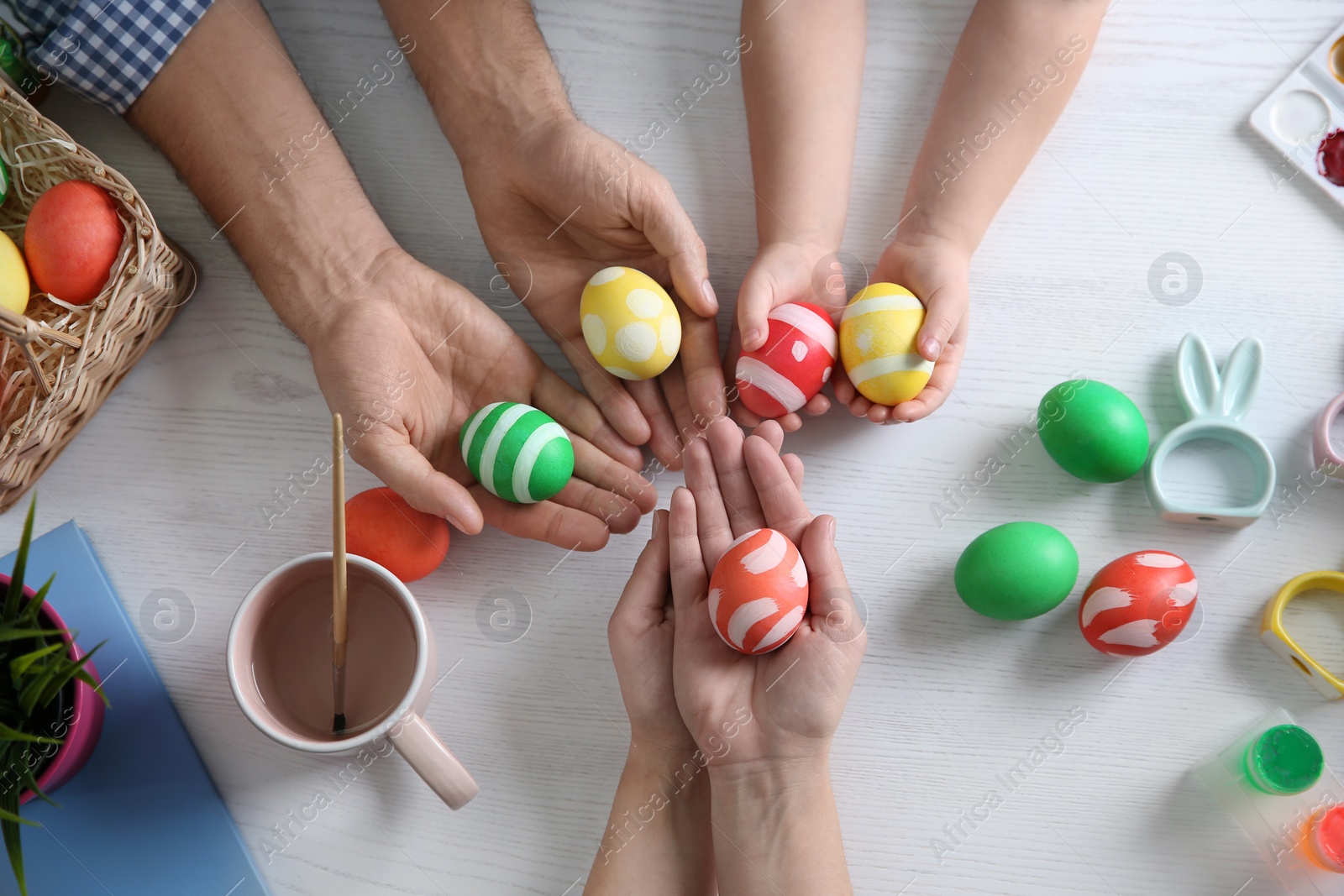 Photo of Father, mother and their child with painted Easter eggs on wooden background, top view