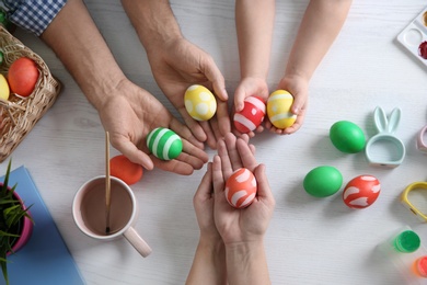 Photo of Father, mother and their child with painted Easter eggs on wooden background, top view