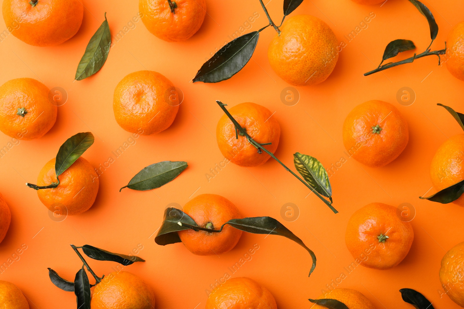 Photo of Fresh ripe tangerines with green leaves on orange background, flat lay
