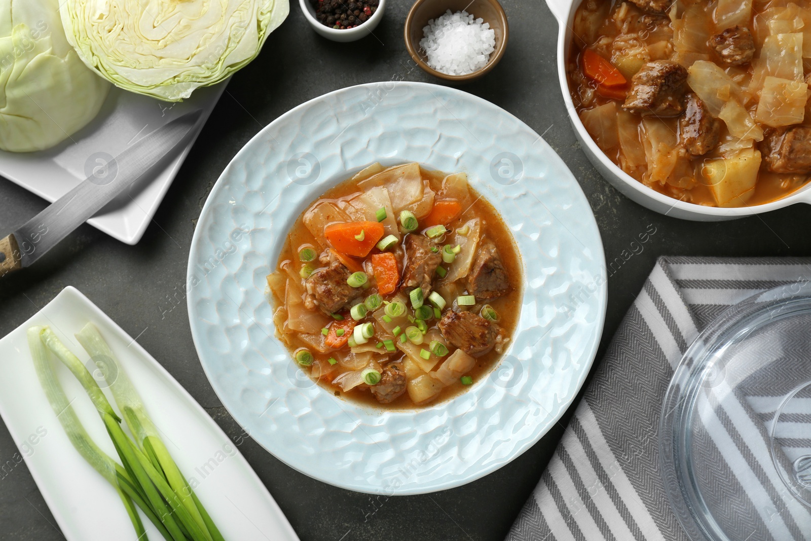 Photo of Tasty cabbage soup and ingredients on grey table, flat lay