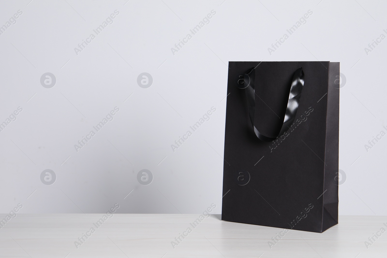 Photo of Black paper bag on white wooden table, space for text