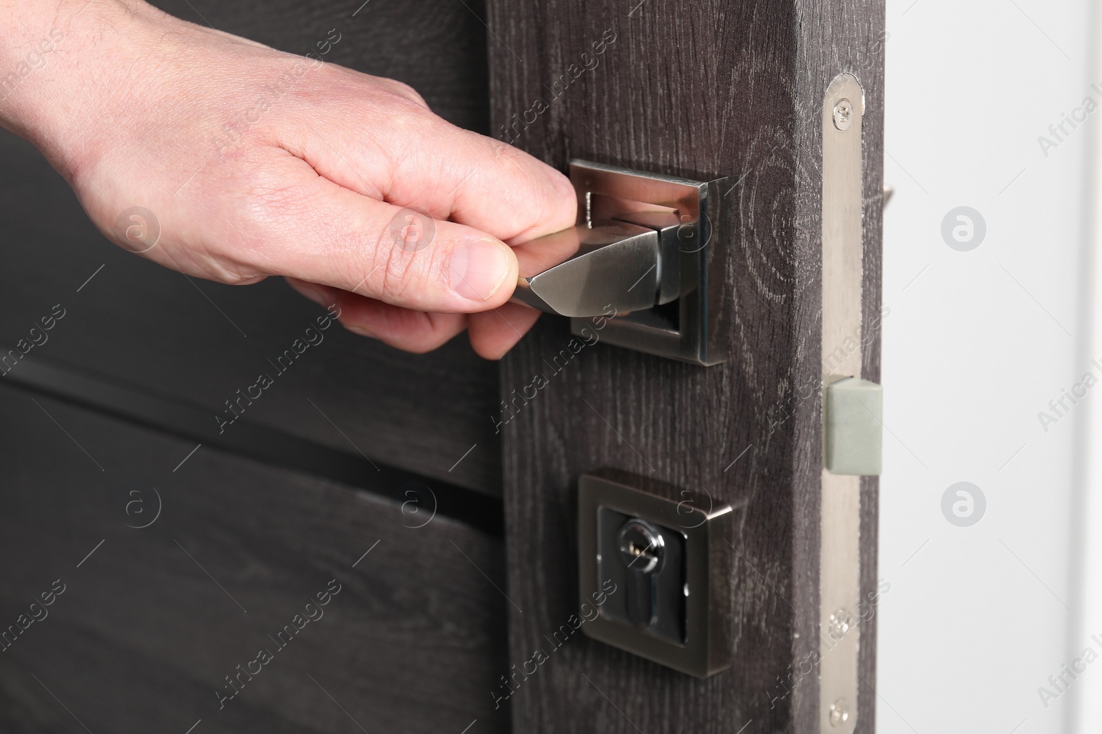 Photo of Man opening wooden door indoors, closeup of hand on handle