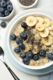 Tasty oatmeal with banana, blueberries and chia seeds served in bowl on white wooden table, flat lay