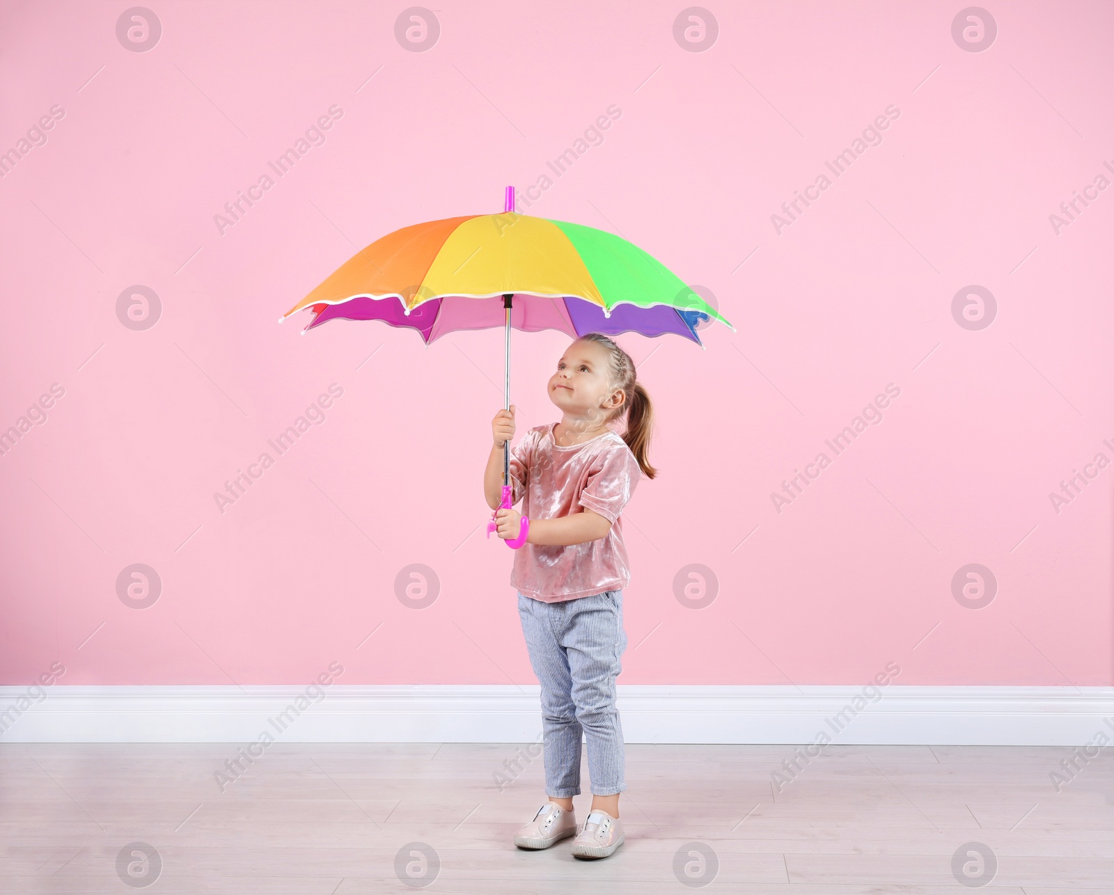 Photo of Little girl with rainbow umbrella near color wall