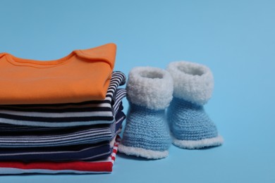 Stack of clean baby clothes and small booties on light blue background