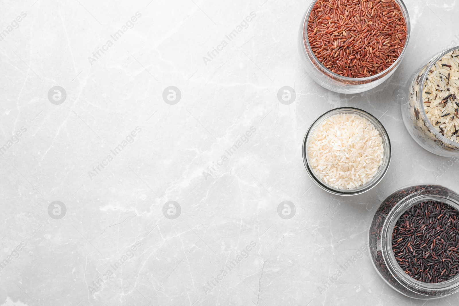 Photo of Brown and polished rice on grey marble table, flat lay. Space for text