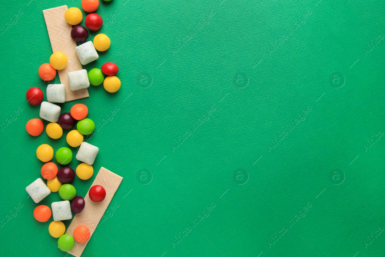 Photo of Different tasty chewing gums on green background, flat lay. Space for text