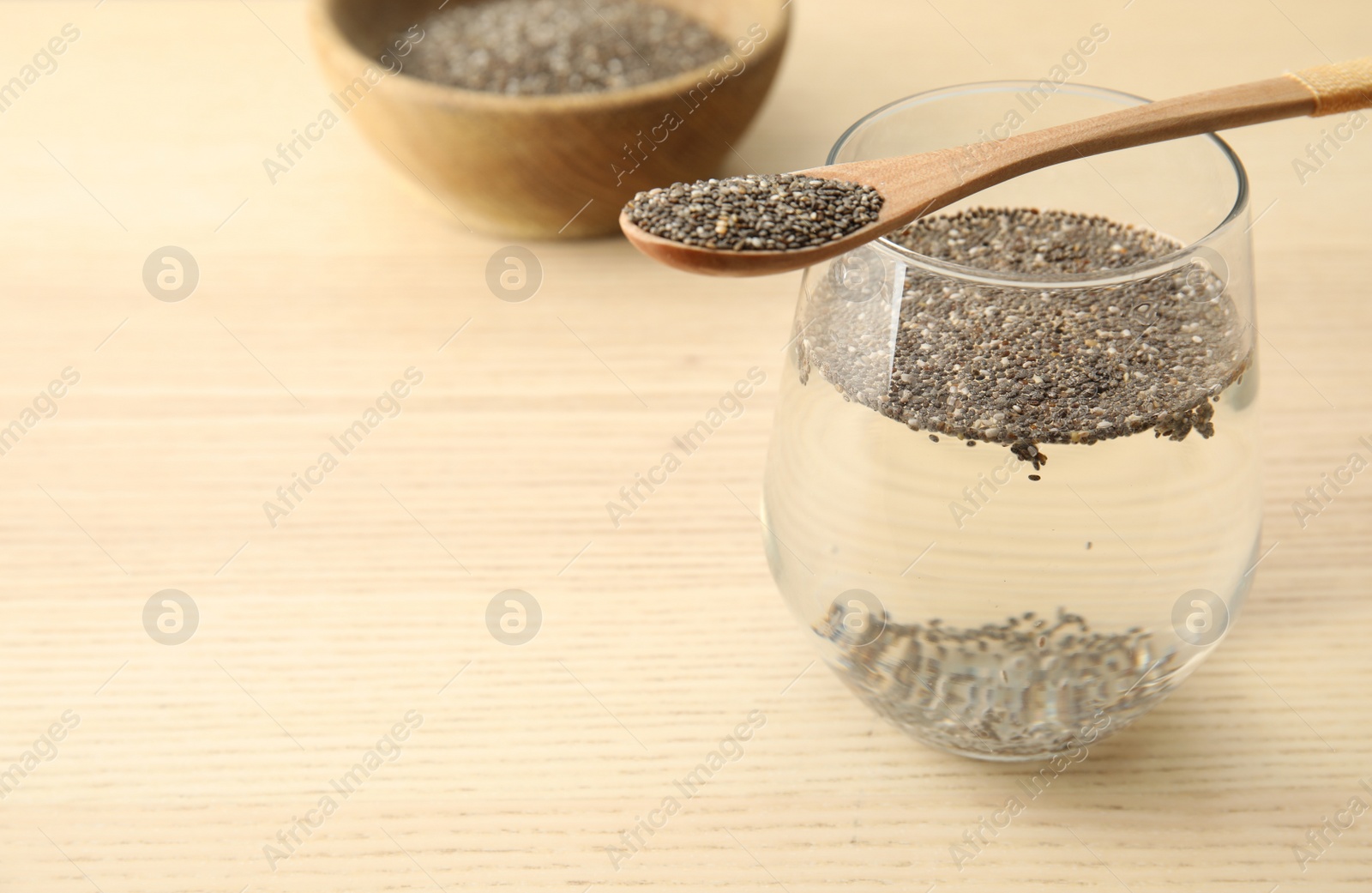 Photo of Glass of water with chia seeds and spoon on wooden background, space for text