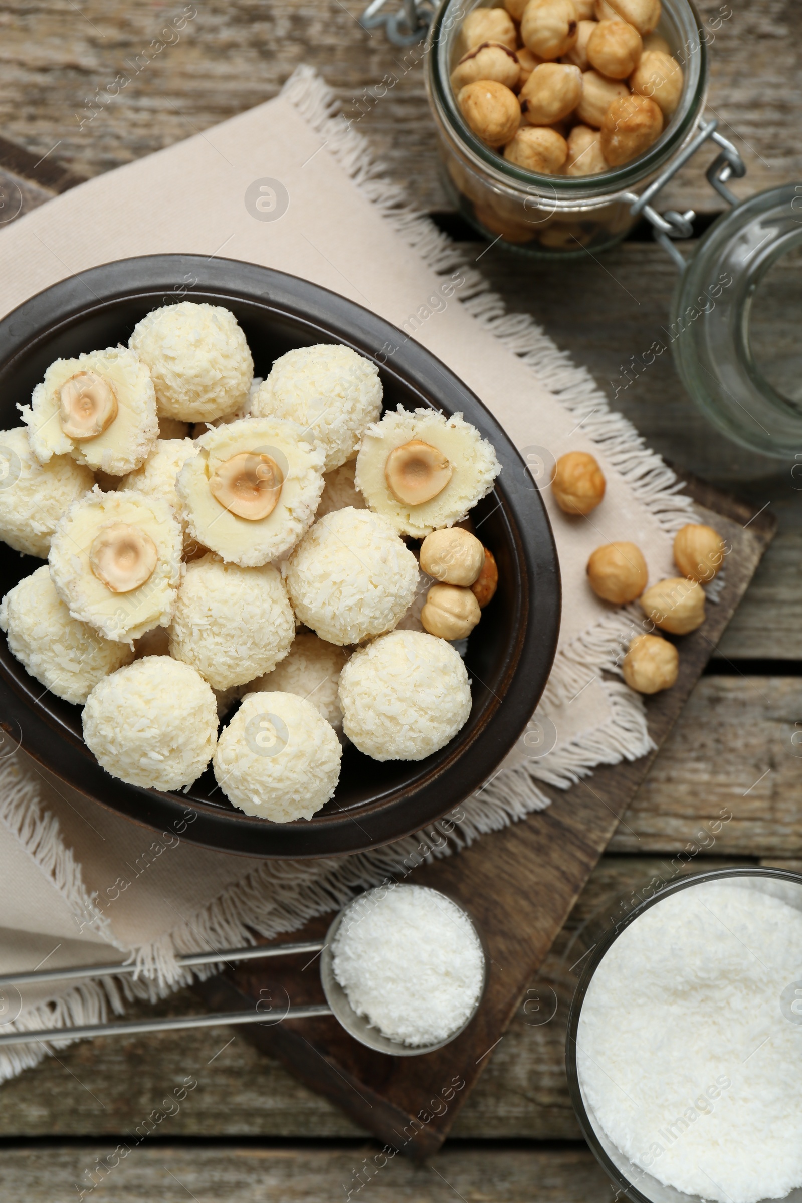 Photo of Delicious candies with coconut flakes, hazelnut and ingredients on wooden table, flat lay